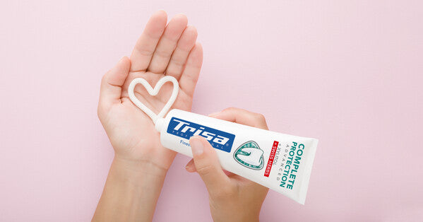 Hand holding TRISA toothpaste for a close-up view of the tube and its Swiss-made formulation.